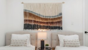 Una camera d'albergo con due letti, un tavolino con una lampada e un elemento decorativo a parete.