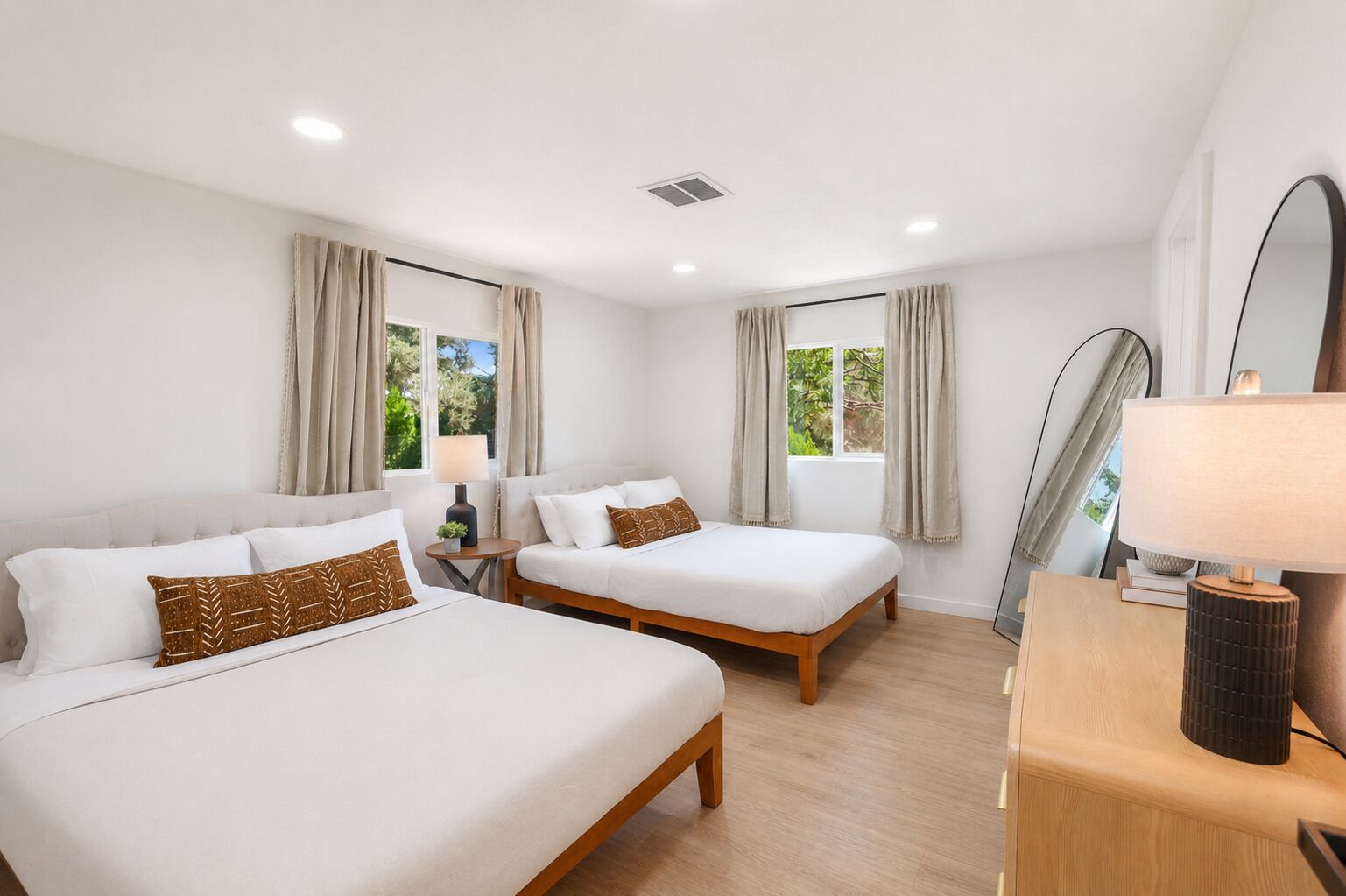 A hotel room with two beds, a bedside table, a lamp, and a mirror.
