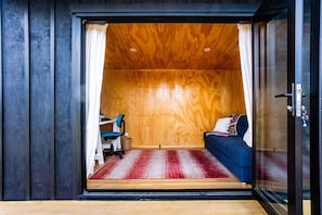 A room with a wooden ceiling, a bed with a blue cover, a desk with a chair, and a red and white striped rug. - Long Bush Nook - Marinborough (Greytown)