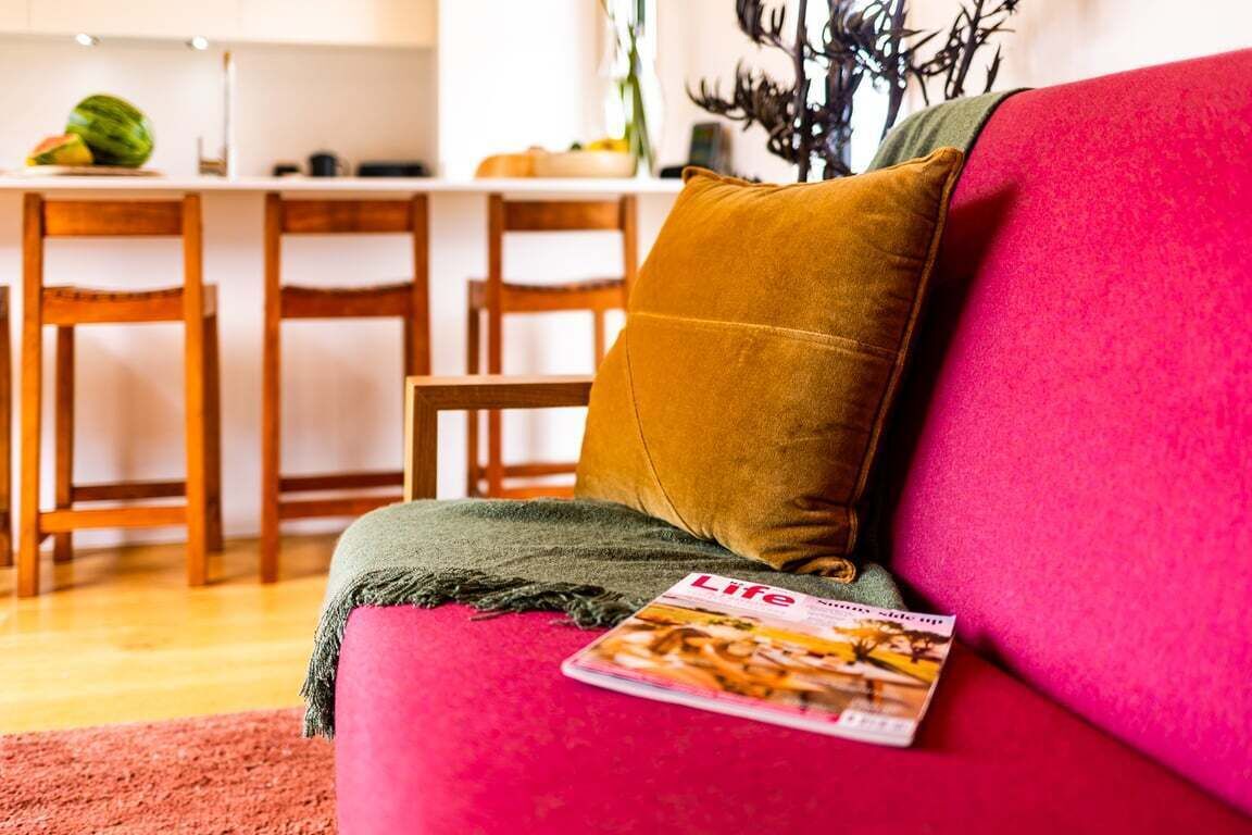 A living room with a red sofa, a mustard-colored pillow, and a magazine on the armrest.