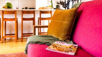 A living room with a red sofa, a mustard-colored pillow, and a magazine on the armrest.