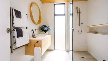 A modern bathroom with a glass shower enclosure, a wooden vanity, a round mirror, and a view of the outdoors.