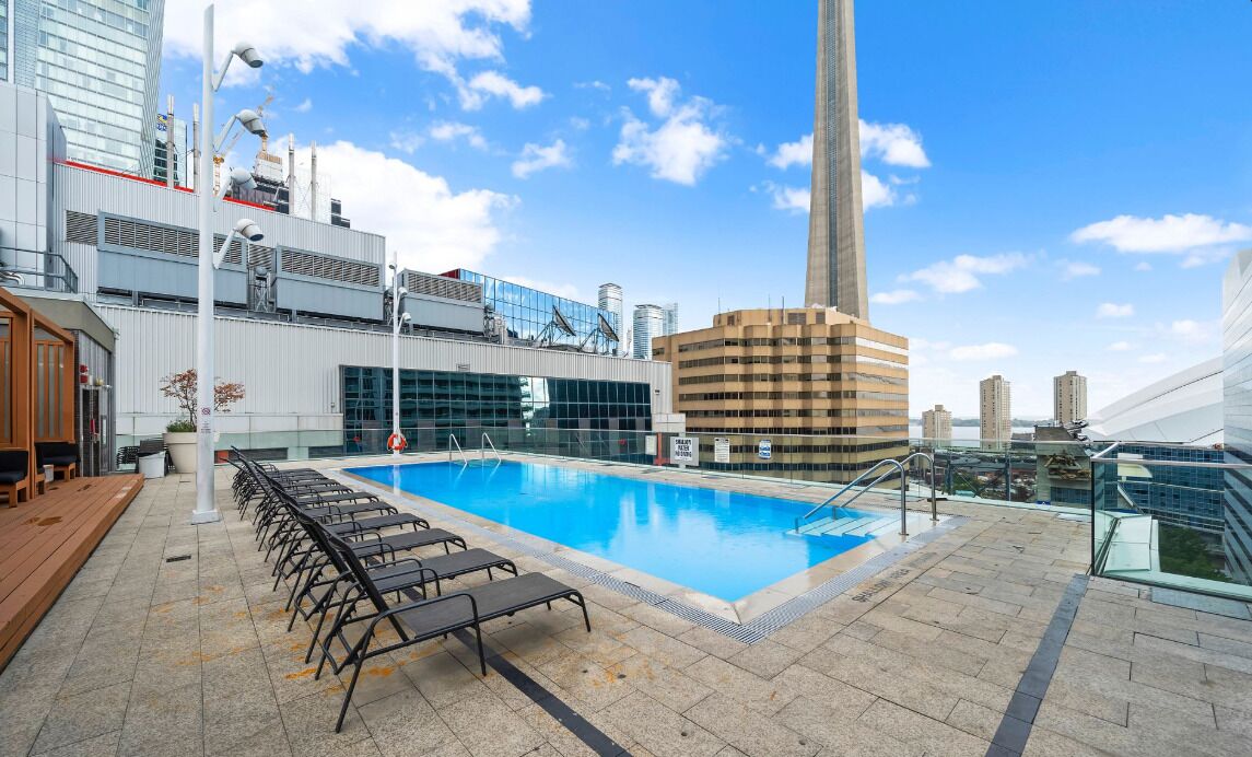 A rooftop pool with lounge chairs, a glass balustrade, and modern buildings in the background.