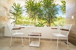 A balcony with two white chairs, a small table, and a view of lush greenery. - 2 King Beds | Rooftop Pool | Walk to Beach & 5th Ave (Playa del Carmen)