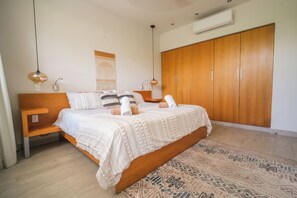 Ein Schlafzimmer mit einem hölzernen Bett, einem Kleiderschrank, einem gemusterten Teppich und Pendelleuchten.