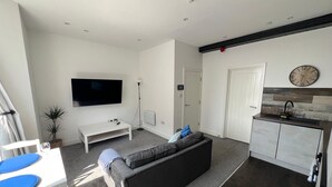 A modern living room with a grey sofa, a flat-screen TV, a white coffee table, and a small plant. - Stylish 1-Bed Flat Central Cardiff Bay View (Cardiff)