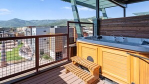 Un terrazzo in legno con vasca idromassaggio e zona relax, con vista su un paesaggio montuoso.