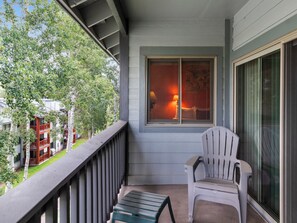 A balcony with a view of a building and trees, a window with blinds, and two chairs. - Snow Flower 124 | Ski-In/Ski-Out | Loft | Pools & Hot Tub (Park City)
