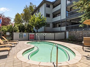 A swimming pool with a diving board, surrounded by lounge chairs, and a stone wall. - Snow Flower 124 | Ski-In/Ski-Out | Loft | Pools & Hot Tub (Park City)