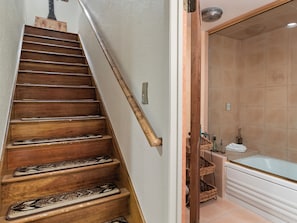 Eine Holztreppe mit Handlauf führt zu einem Badezimmer mit Badewanne und einer gefliesten Duschkabine.