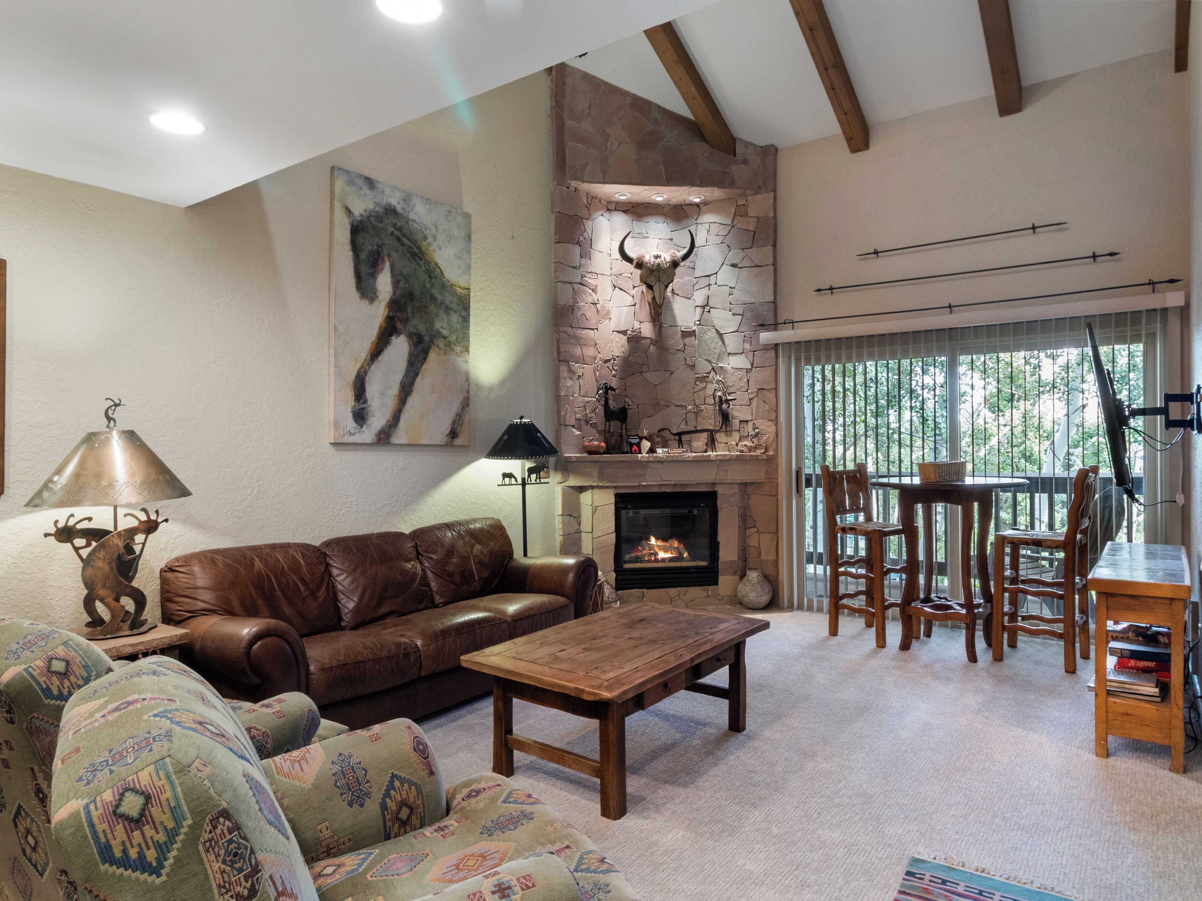 A cozy living room with a fireplace, leather sofa, patterned armchair, and a dining area with wooden furniture.