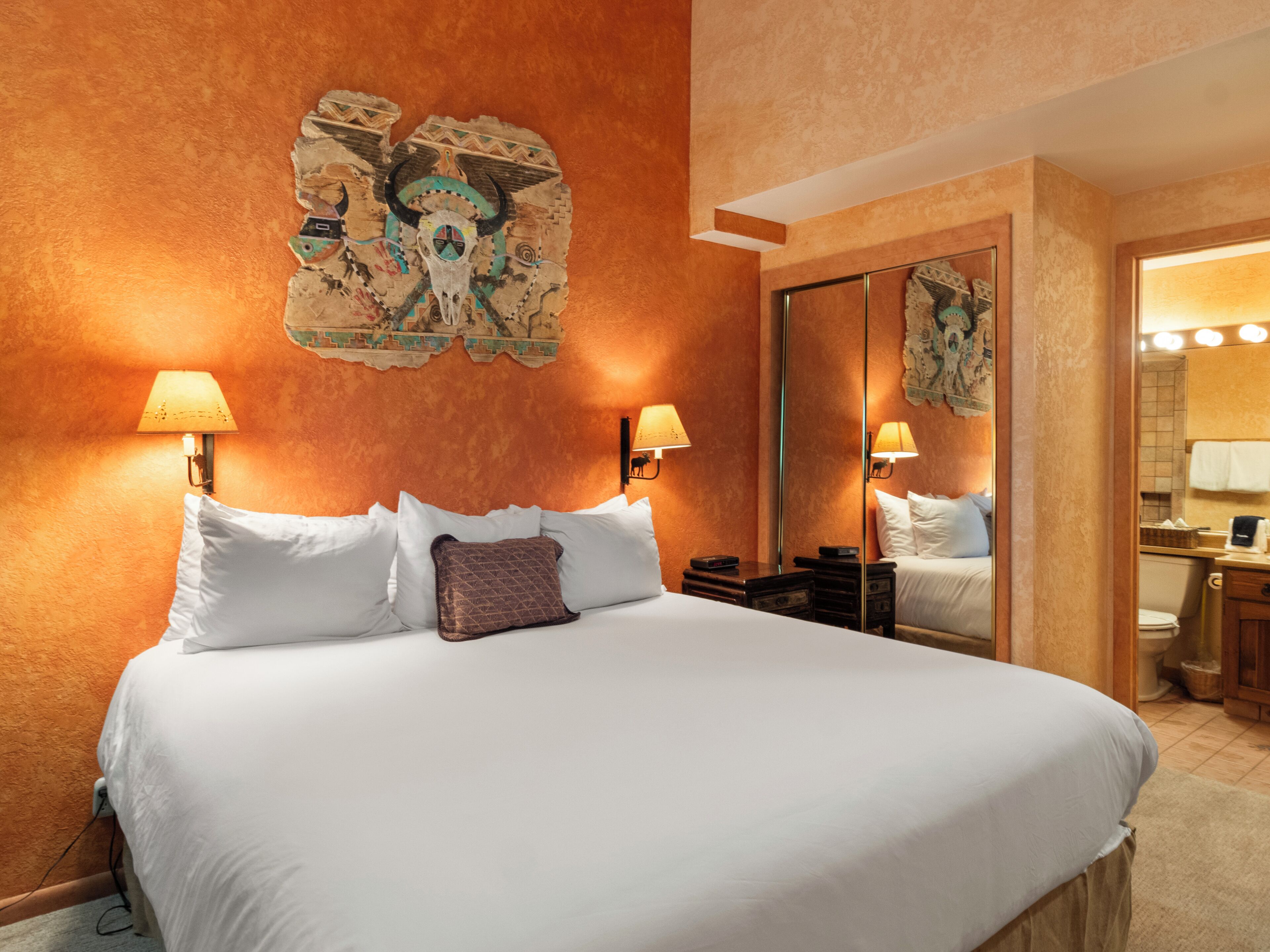 Ein Hotelzimmer mit einem großen Bett, zwei Nachttischlampen, einem Spiegel und einem Wandbild.