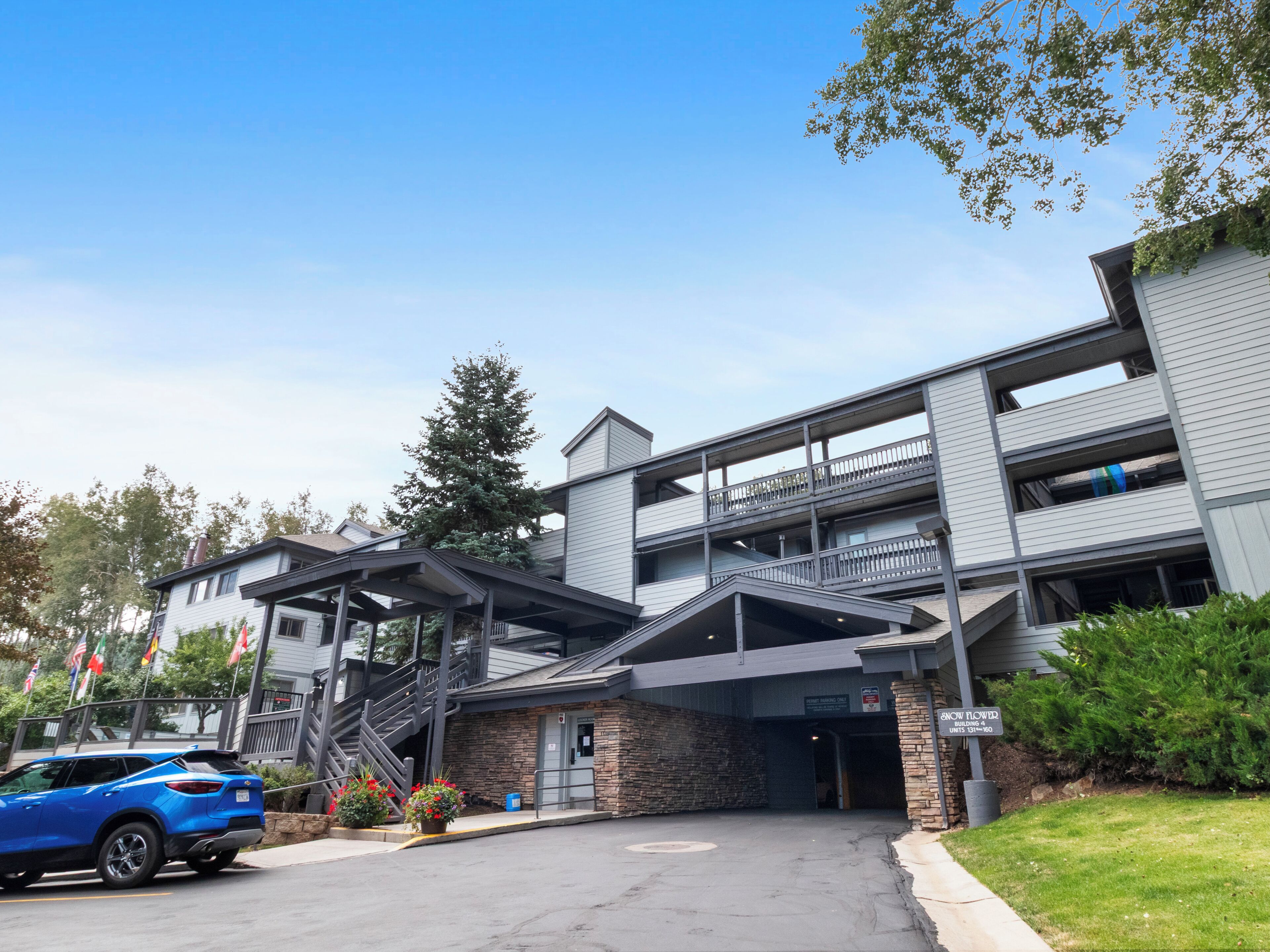 A multi-story building with a covered entrance, outdoor seating area, and a parking lot with a blue car.