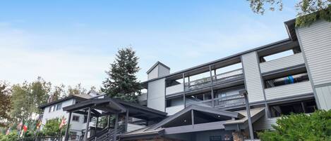 A multi-story building with a covered entrance, outdoor seating area, and a parking lot with a blue car.