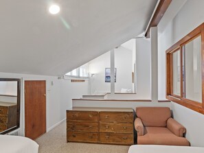 Une chambre à coucher avec une commode en bois, un fauteuil rose et un grand miroir.