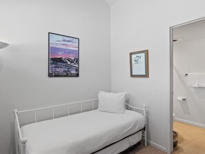 Ein Einzelzimmer mit einem Bett aus weißem Metall, einer weißen Matratze und einem an der Wand befestigten Poster mit einer Berglandschaft.
