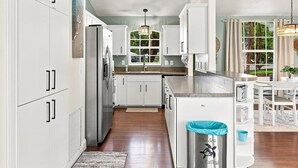 A kitchen with white cabinets, a stainless steel refrigerator, a window with a view, and a trash can with a message. - Welcome to The Sea Is Calling 2.0 (Sarasota)