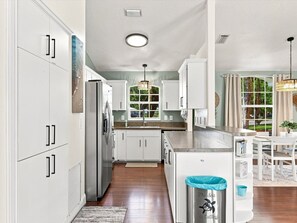 A kitchen with white cabinets, a stainless steel refrigerator, a window with a view, and a trash can with a message. - Welcome to The Sea Is Calling 2.0 (Sarasota)