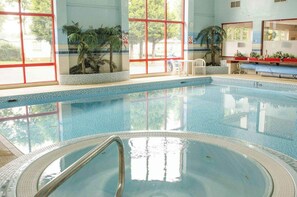 Una piscina con agua azul cristalina, rodeada de ventanas de marcos rojos y plantas de interior.