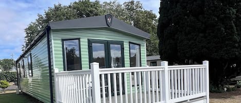 Uma casa móvel térrea com varanda branca e telhado verde.