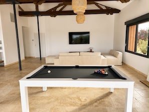 Ein Billardtisch in einem modernen Wohnzimmer mit einer Couch und einem Fernseher.