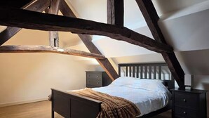 Quarto com teto inclinado, estrutura de cama de madeira, mesa de cabeceira e um criado-mudo.
