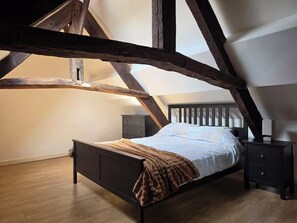 Ein Schlafzimmer mit schrägem Dach, einem Holzbettgestell, einem Nachttisch und einem Beistelltisch.