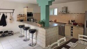Uma cozinha com ilha central, banquetas de bar, uma mesa de jantar e um sapateiro.