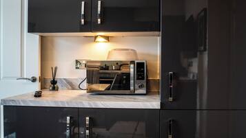 A kitchen with a built-in microwave oven, a coffee maker, and a small table with a remote control and a decorative item.