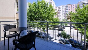 Ein Balkon mit Tisch und Stühlen, der auf eine Straße mit parkenden Autos und Gebäuden blickt.