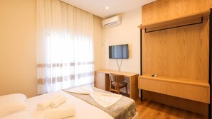 A hotel room with a bed, a desk, a chair, a TV, and a wardrobe.