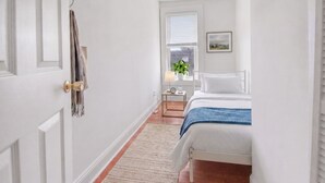 Um quarto com cama, mesa de cabeceira, planta e um quadro na parede.