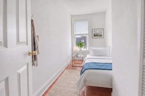 Una camera da letto con un letto, un comodino, tende alla finestra, una pianta e un quadro appeso al muro.