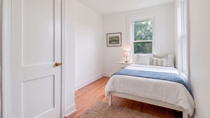 Quarto com cama, mesa de cabeceira, abajur, janela e porta.