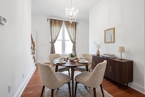 Una sala da pranzo con un tavolo rotondo apparecchiato per quattro persone, un lampadario, un mobile contenente libri e uno specchio a parete.