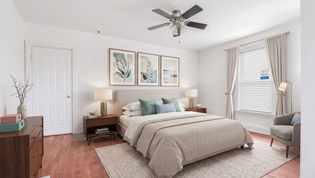 Quarto com cama, mesas de cabeceira, ventoinha no teto, janela com cortinas e obras de arte na parede.