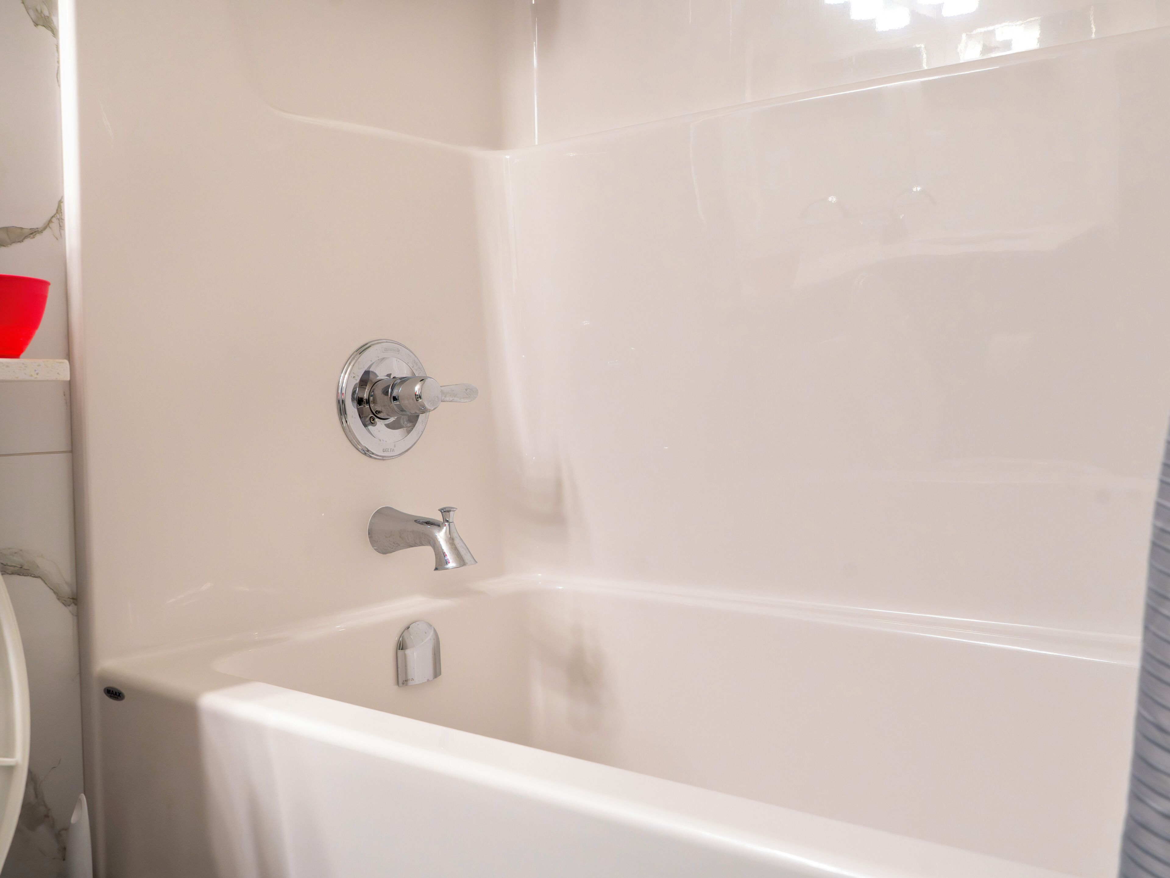 Una bañera con cabezal de ducha y grifo, un panel de control montado en la pared y una esquina de un baño con pared de azulejos blancos.