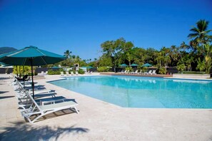 A swimming pool with lounge chairs and umbrellas, surrounded by palm trees and greenery. - Charming 2-bedroom apartment with AC in perfect Puerto Plata (Puerto Plata)