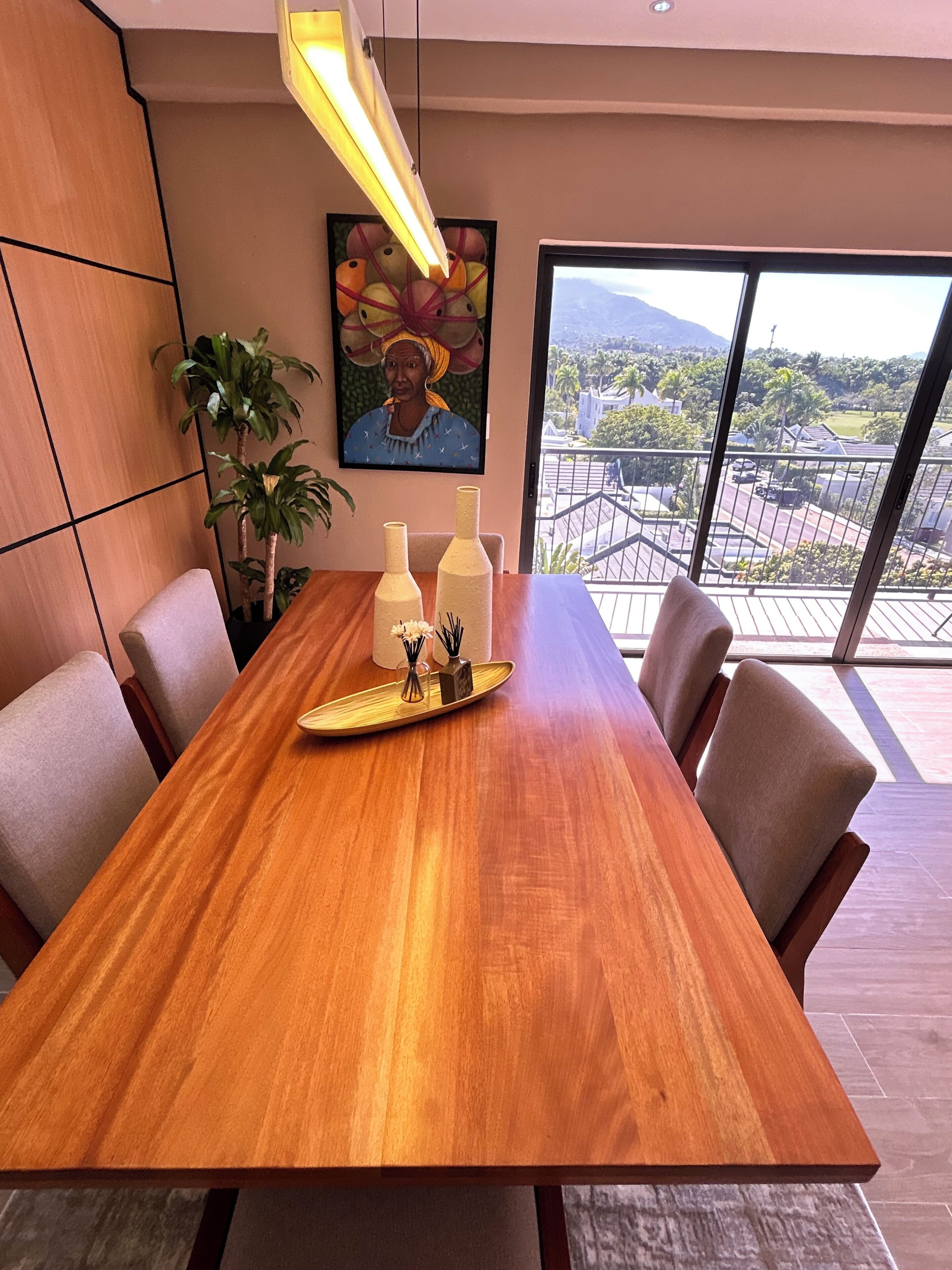 A conference room with a wooden table, chairs, a potted plant, a painting, and a view of the outdoors.