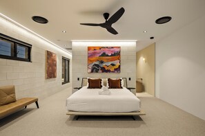 A modern hotel room with a large bed, a ceiling fan, and artwork on the walls. - Stone & Tide by Aryve (Runaway Bay)