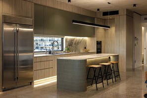 A modern kitchen with a stainless steel refrigerator, a marble backsplash, and a built-in island with bar stools. - Stone & Tide by Aryve (Runaway Bay)