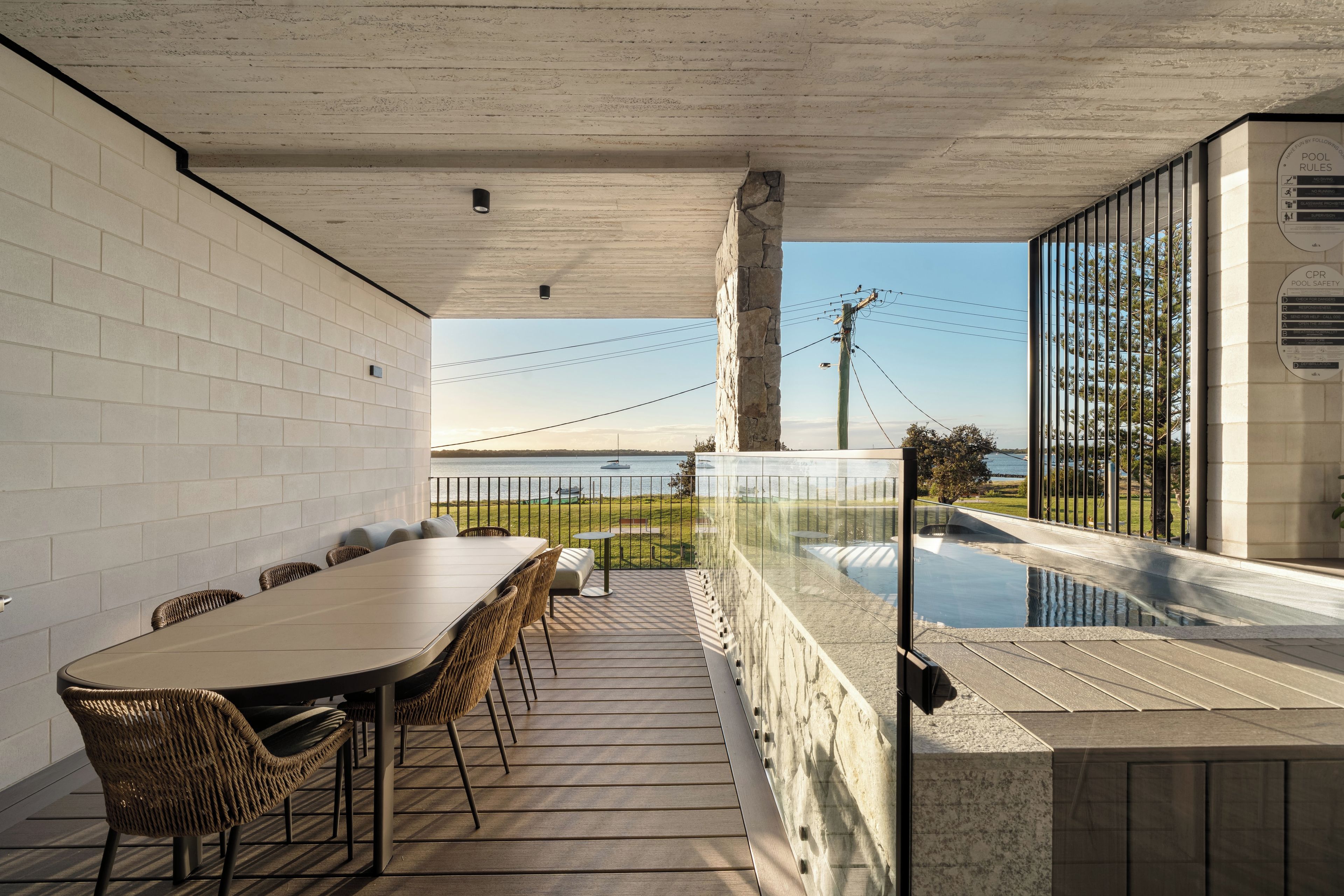 Een zwembad met een tafel, stoelen, een glazen balustrade en uitzicht op het water.