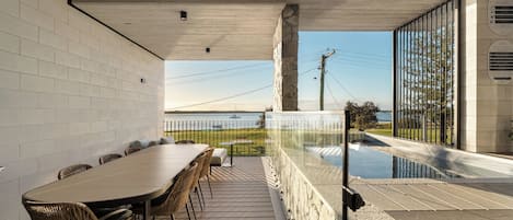 Een zwembad met een tafel, stoelen, een glazen balustrade en uitzicht op het water.