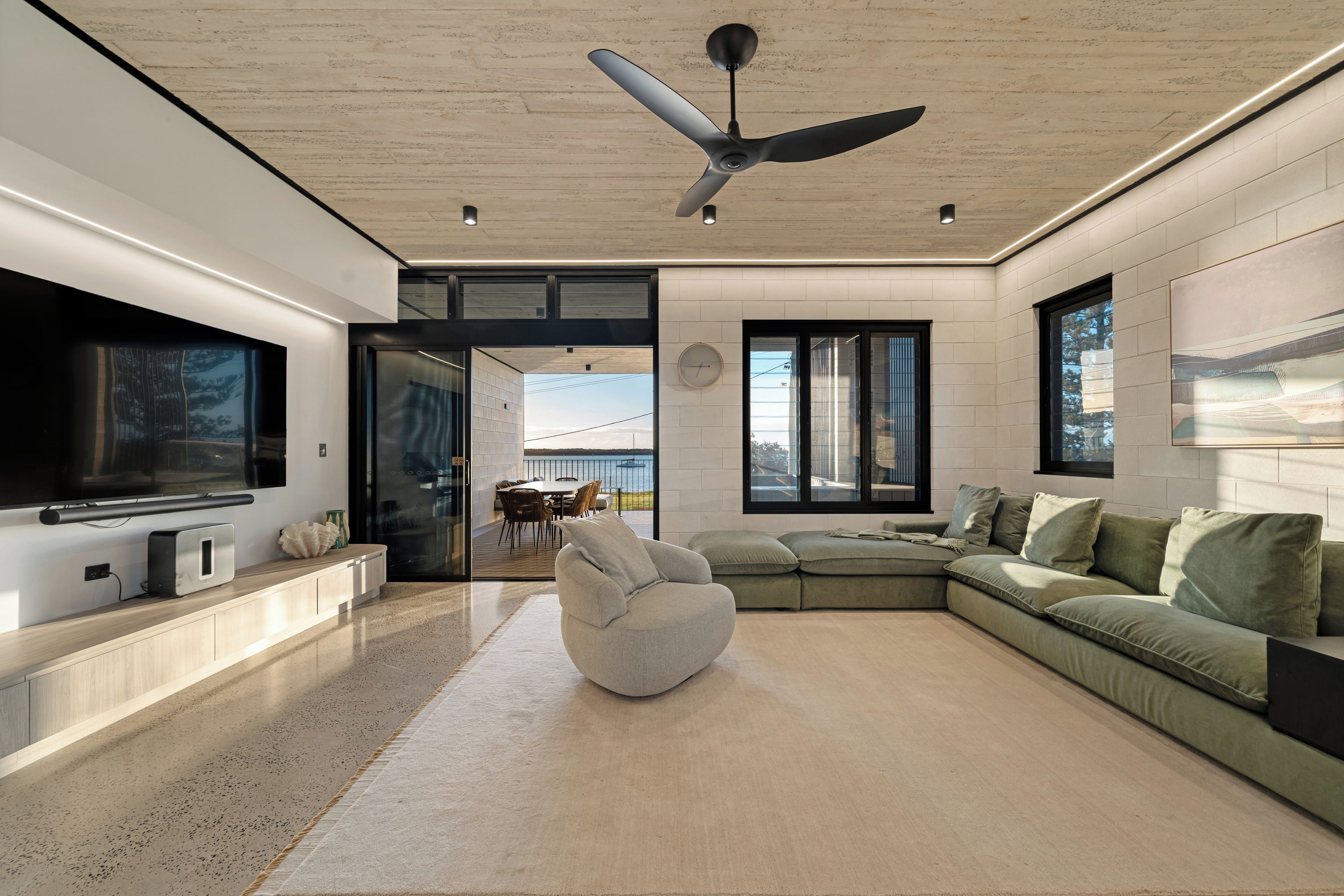 Un salon moderne doté d’un téléviseur à écran plat, d’un ventilateur de plafond et d’une grande fenêtre donnant sur une terrasse.