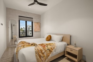Ein Schlafzimmer mit Bett, Nachttisch, Fenster und Deckenventilator.
