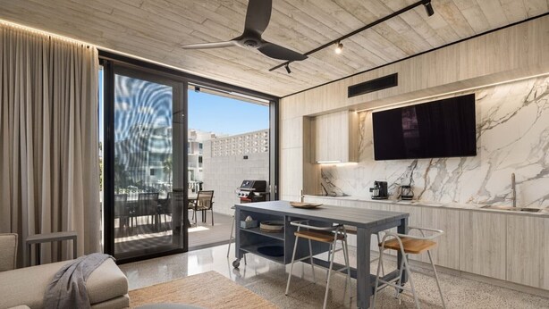 Un salon moderne comprenant un coin repas, un téléviseur à écran plat fixé sur un mur en marbre et une porte-fenêtre coulissante donnant sur une terrasse extérieure.