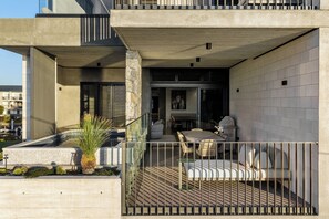 A modern outdoor patio with a dining area, a stone column, and a view of the adjacent building. - Stone & Tide by Aryve (Runaway Bay)