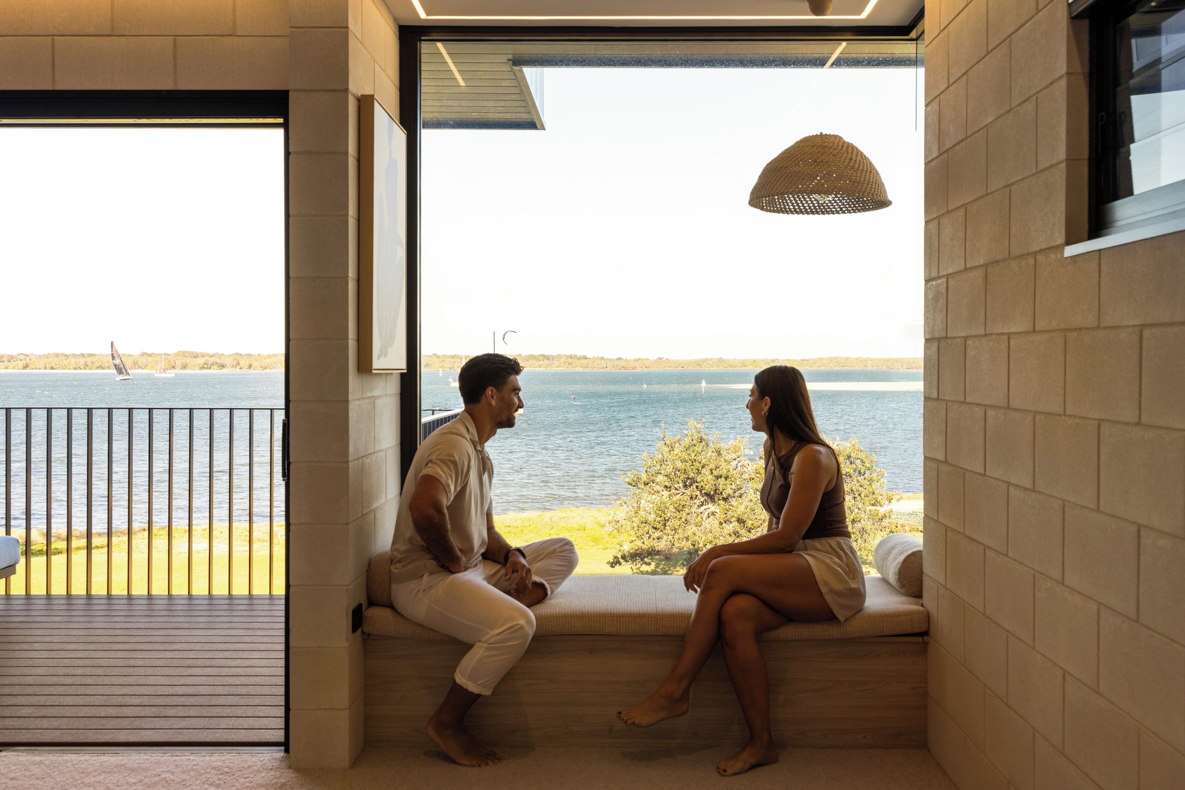 A couple seated on a bench by a window overlooking a body of water.