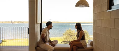 Una pareja sentada en un banco junto a una ventana con vista al agua.