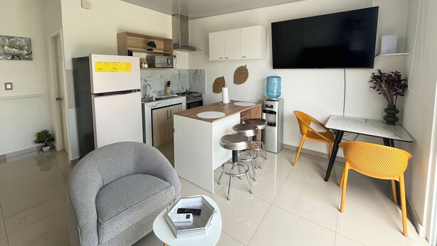 Eine moderne Küche mit Kühlschrank, Mikrowelle und Herd. Es gibt einen Essbereich mit Tisch und Stühlen, einen an der Wand montierten Fernseher sowie einen Wasserspender.